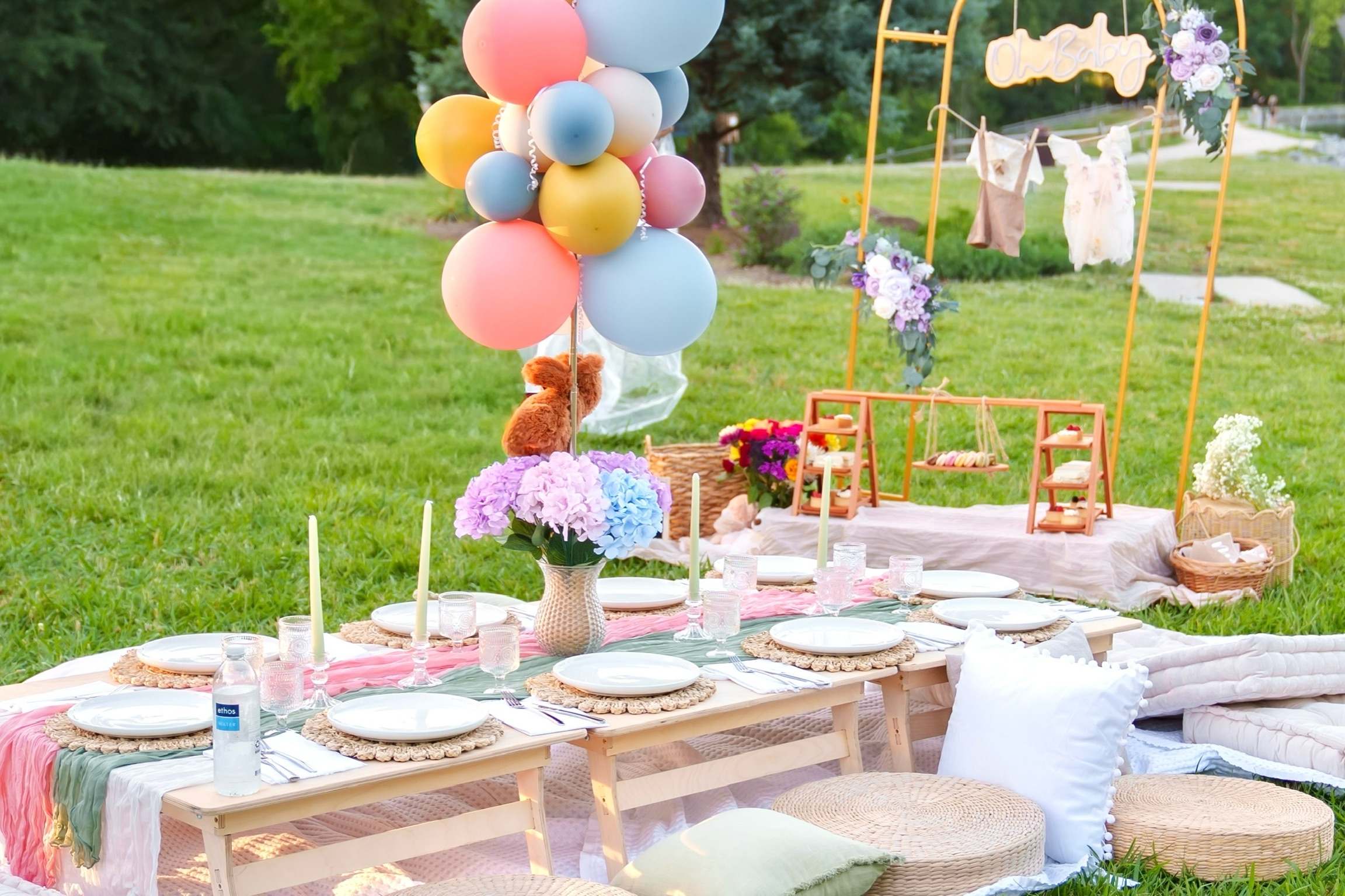 A pastel baby shower picnic with a balloon cluster and a line of baby clothes