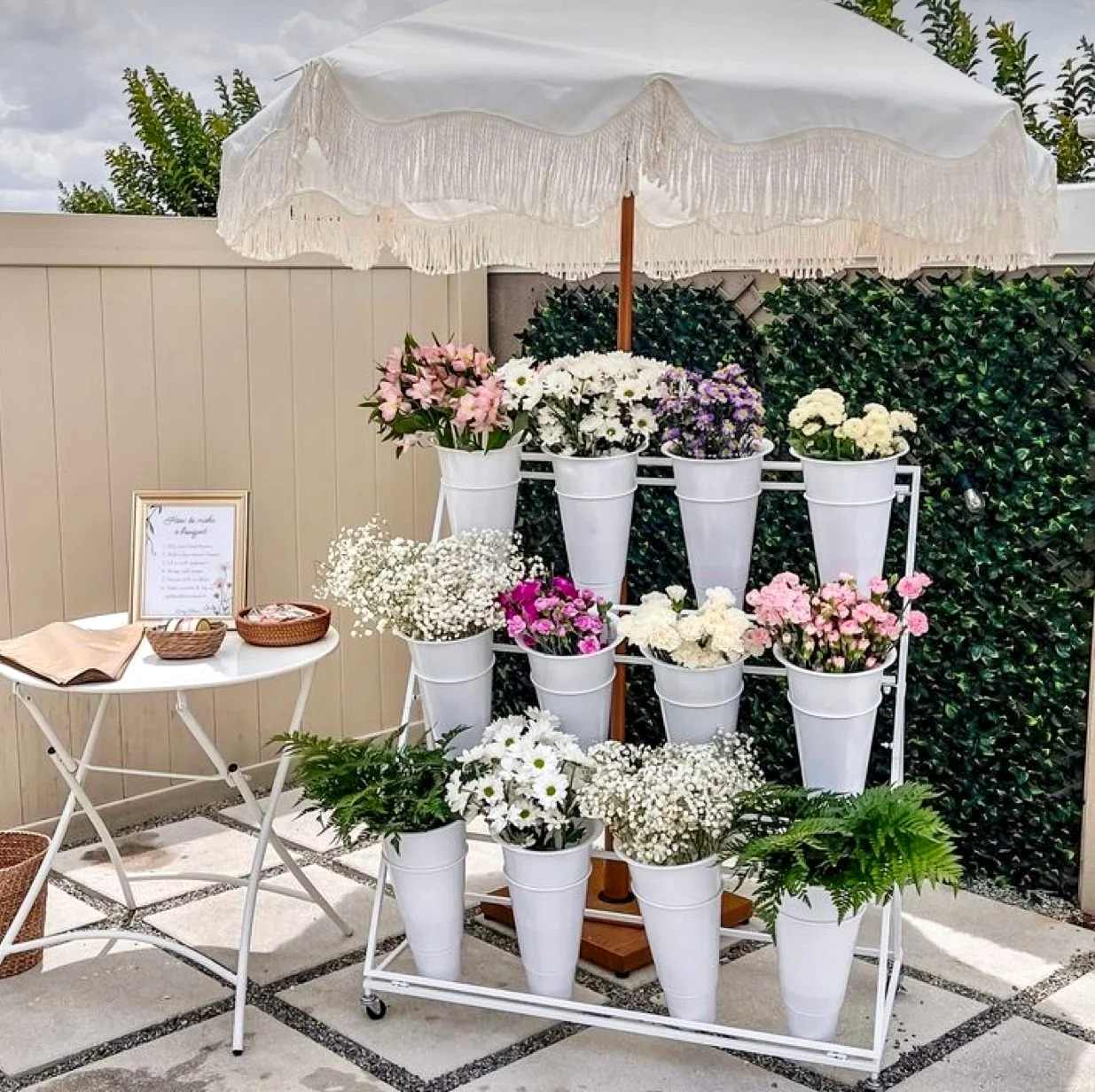 White bloom cart under a fringed umbrella, filled with buckets of fresh flowers