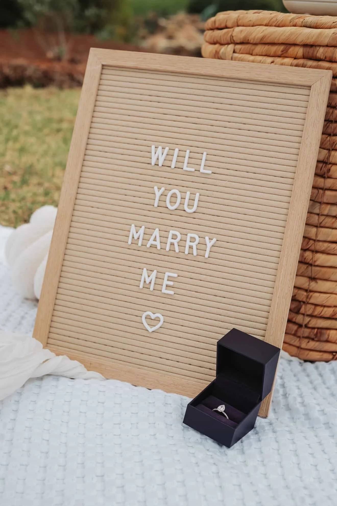 A letter board reading Will you marry me beside a ring box