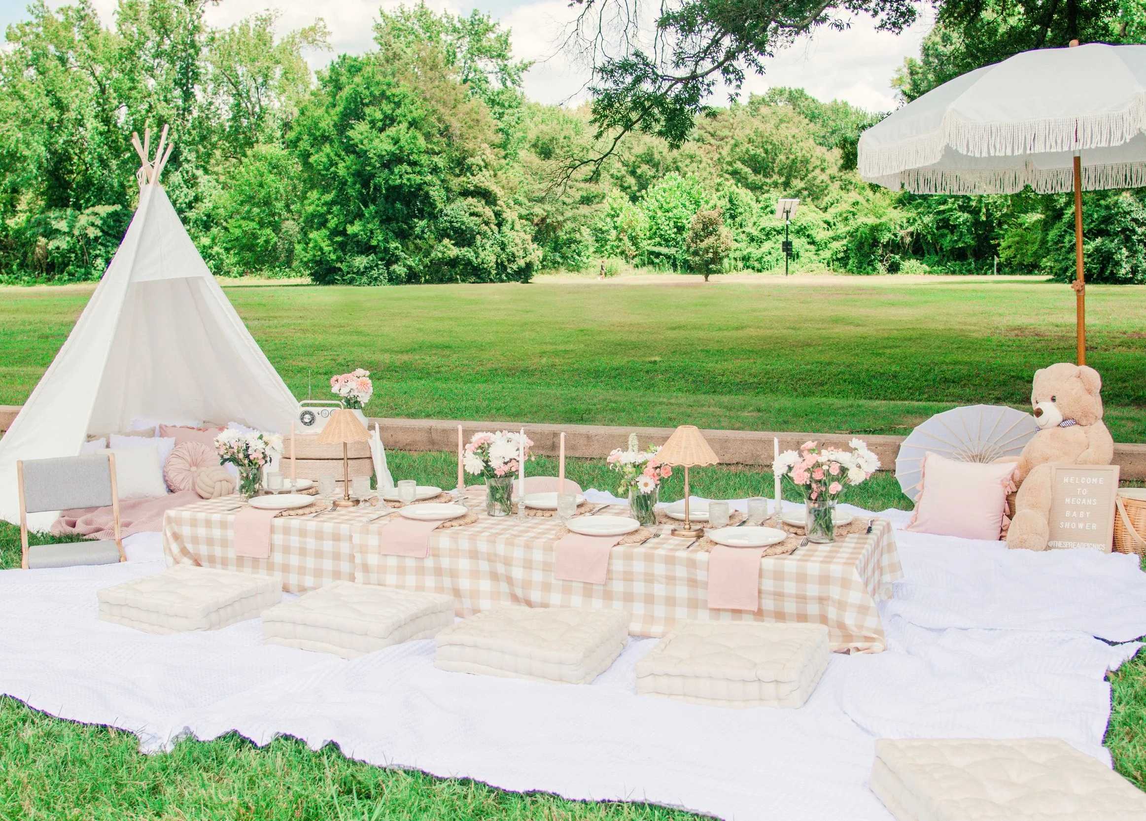 A low picnic table set on a gingham cloth beside a white teepee, under a fringed umbrella
