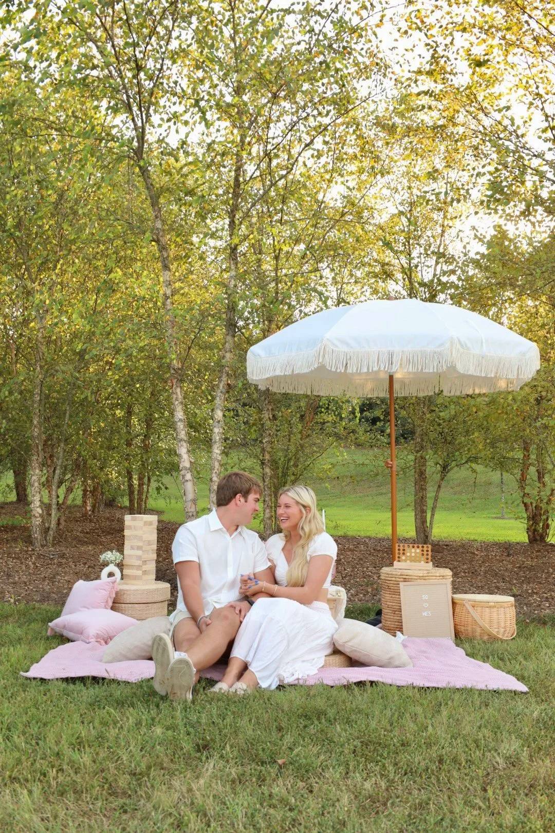 A couple sitting together at a picnic under a white umbrella among trees