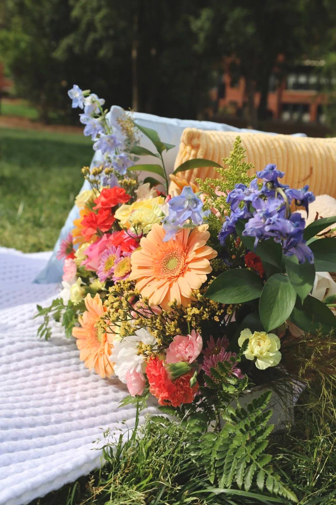 A bright bouquet of gerberas and delphinium resting on a picnic blanket