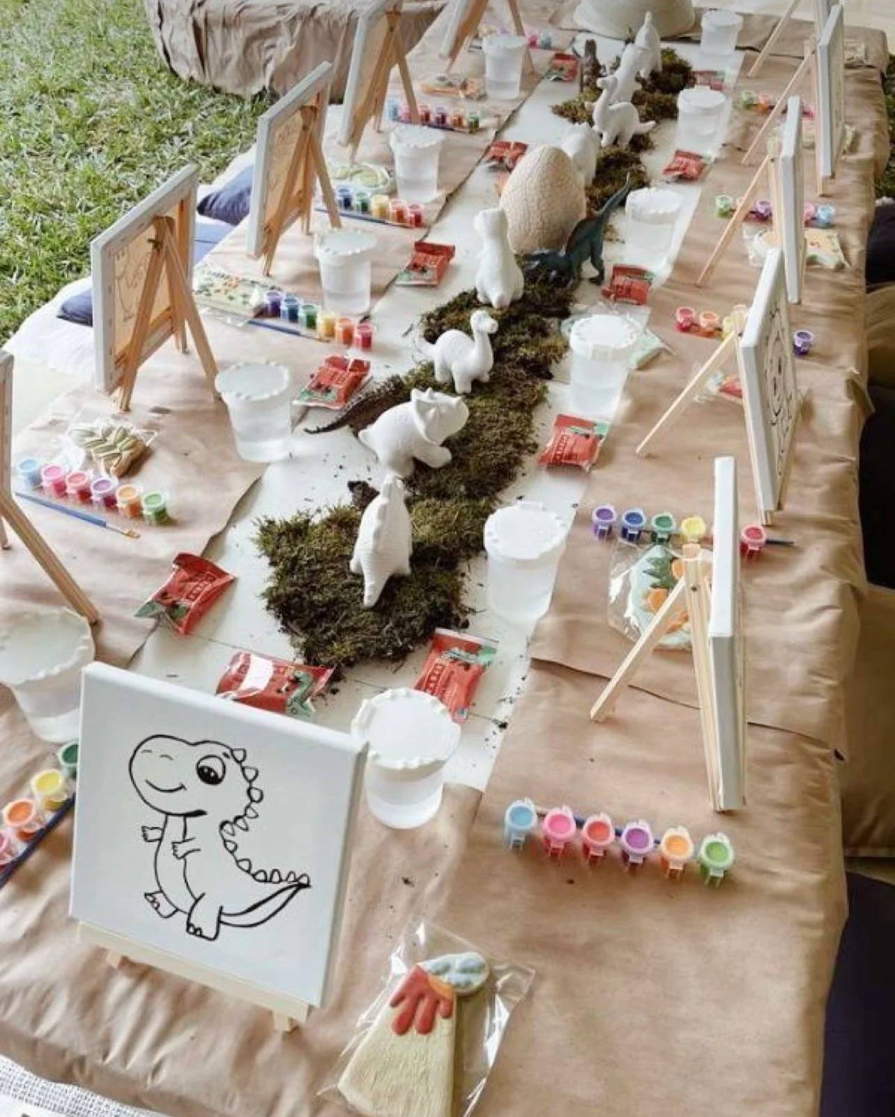 A kids painting party table with canvases, paint cups and a dinosaur sketch