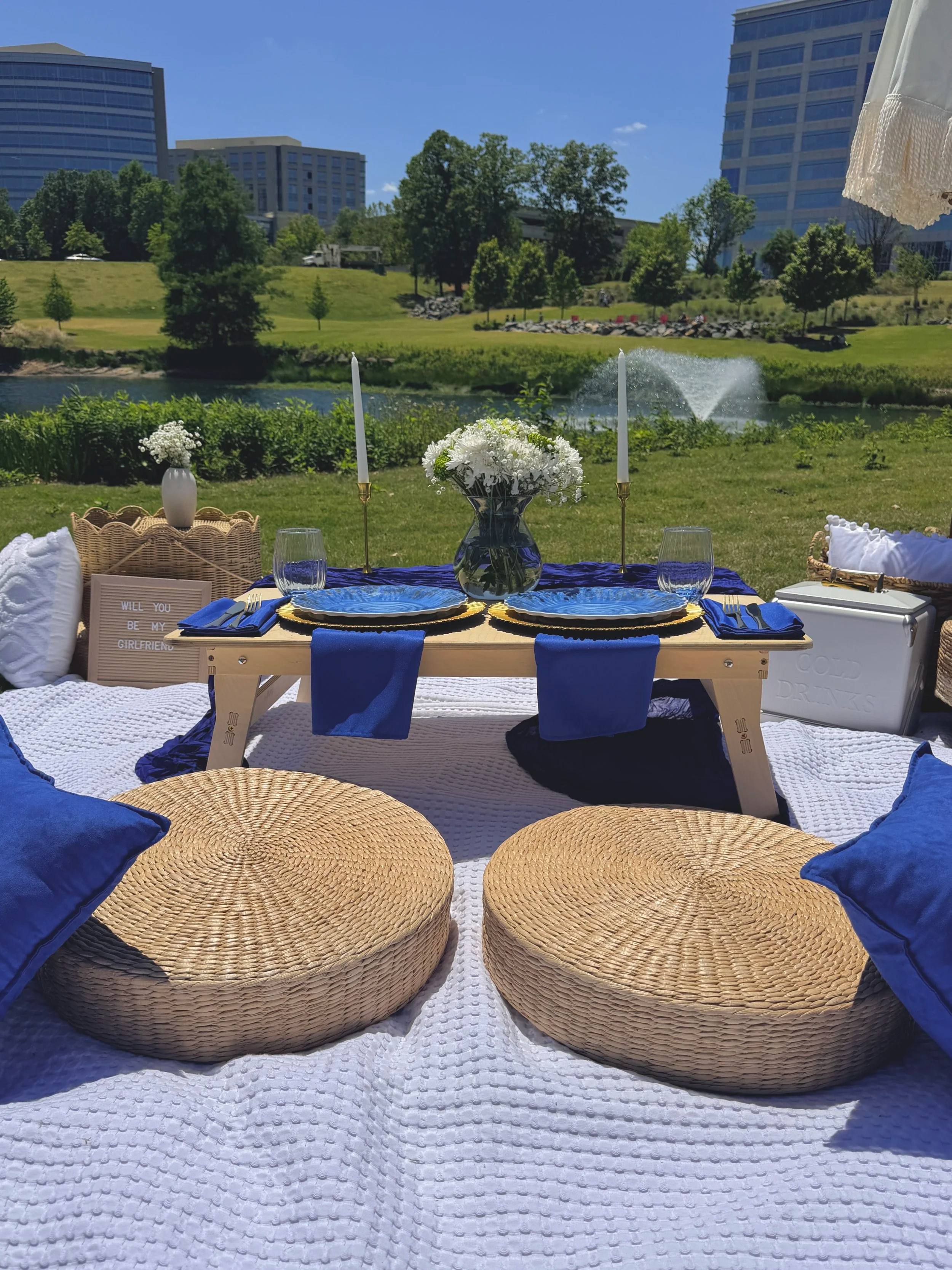 Navy cushions and a low table on a white blanket beside a pond with a fountain