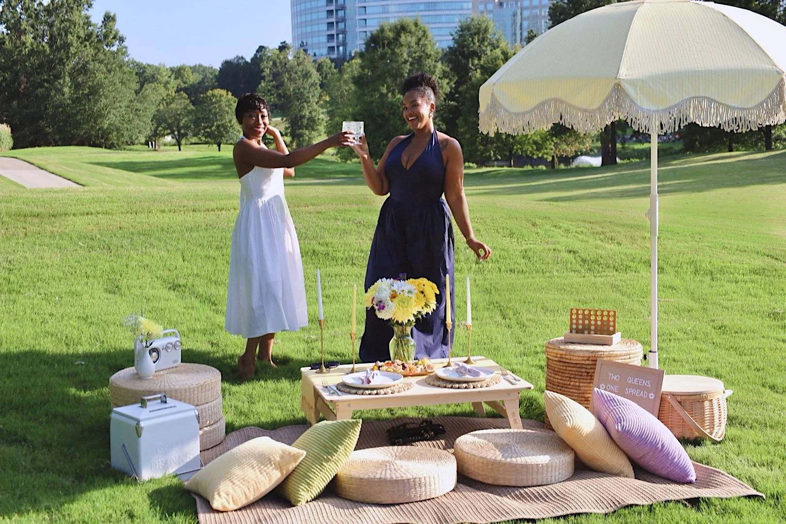 Two guests toasting beside a picnic setup on a wide lawn