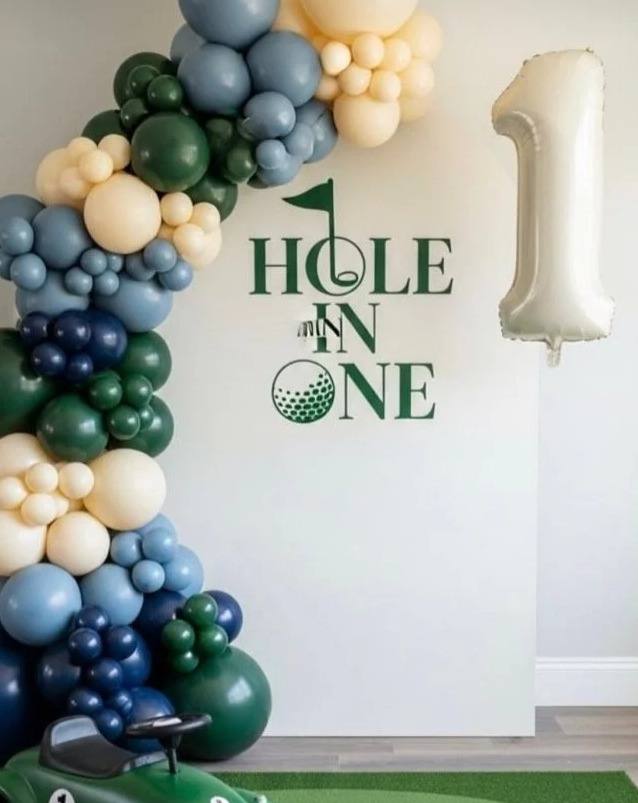Mini-Masters kids party: a Hole In One balloon backdrop in navy, sage and cream beside a toy golf cart