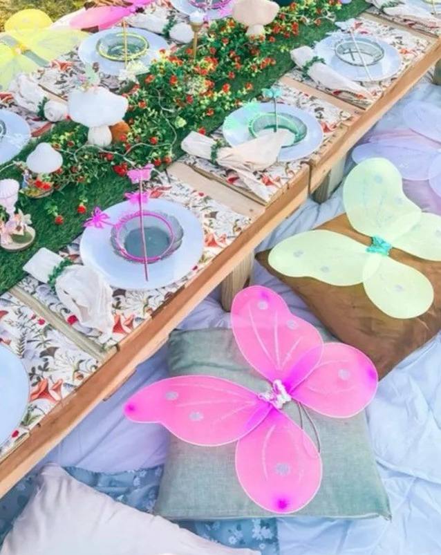 Enchanted Pixie Party: a long low table on the grass with pink and yellow butterfly wings waiting on the cushions