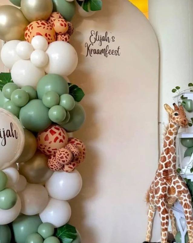 Little Explorers Safari kids party: a sage, white and animal-print balloon arch beside a toy giraffe