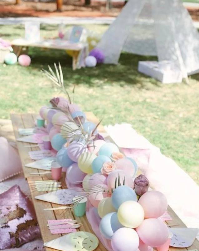 Whimsical Wonderland kids party: a low pallet table on the grass with pastel balloons, cushions and a white teepee behind