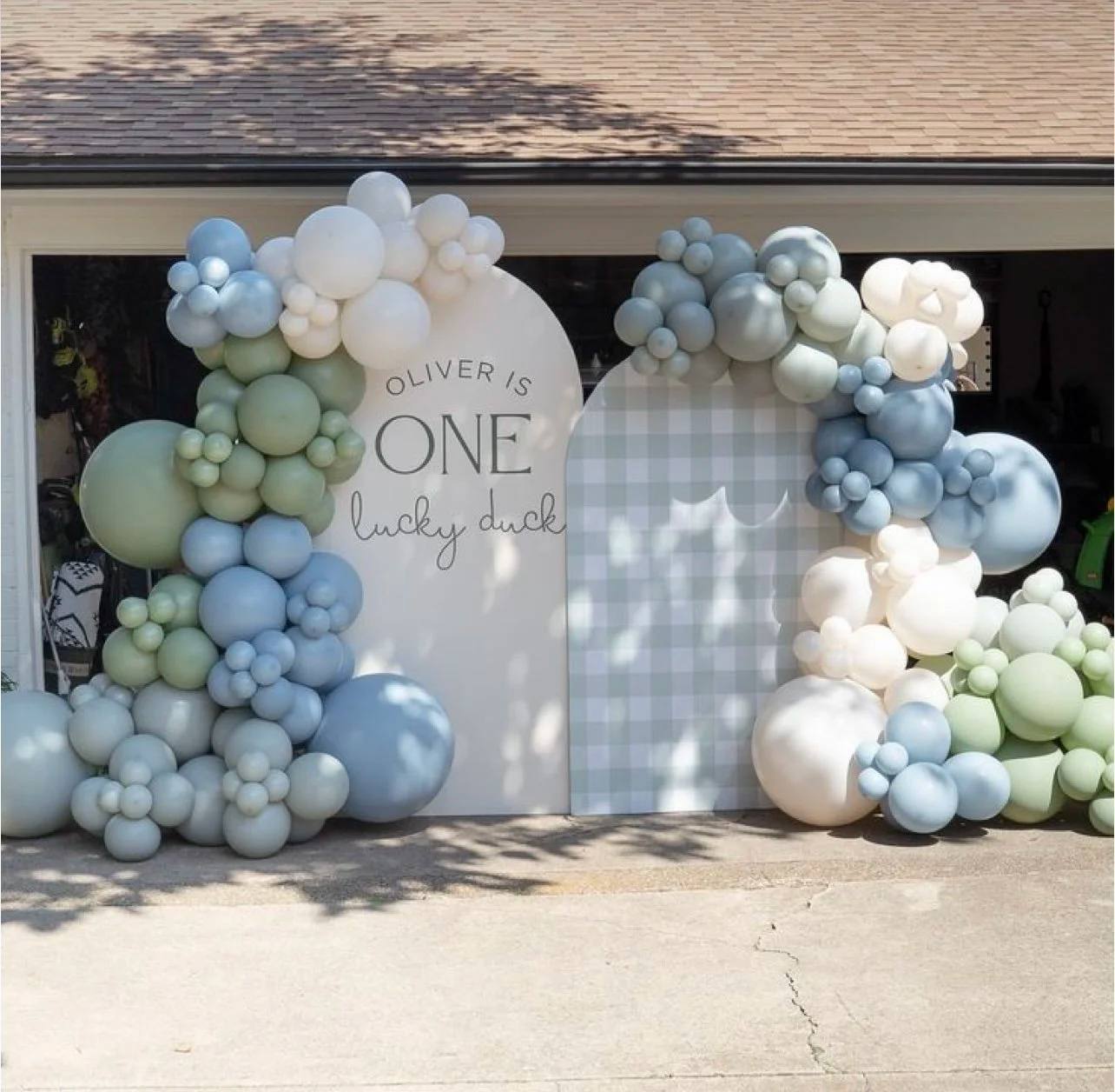 A white arch lettered One Lucky Duck beside a blue gingham arch, framed by blue, sage and cream balloons