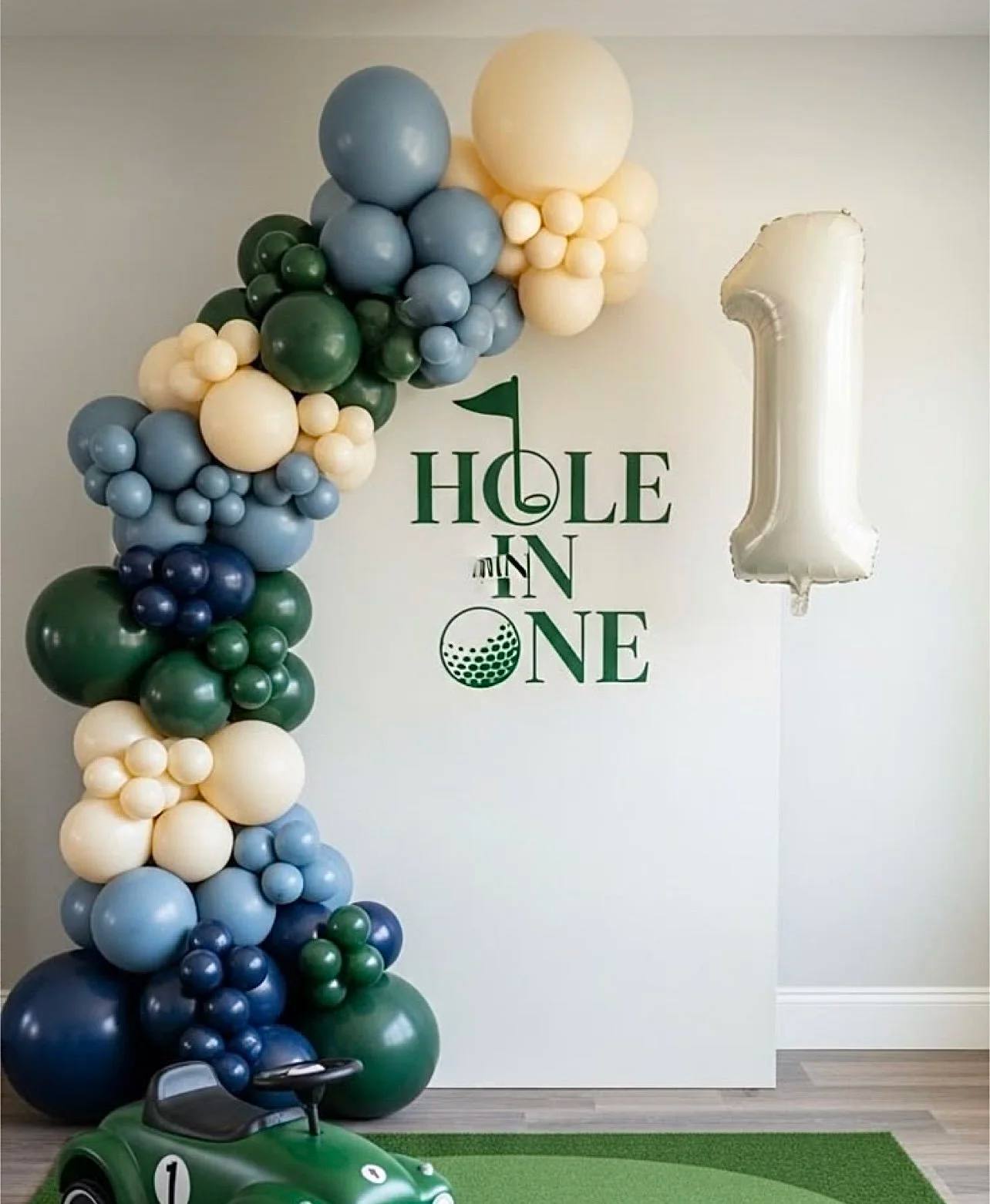 A Hole In One golf backdrop with navy, green and cream balloons and a number one balloon